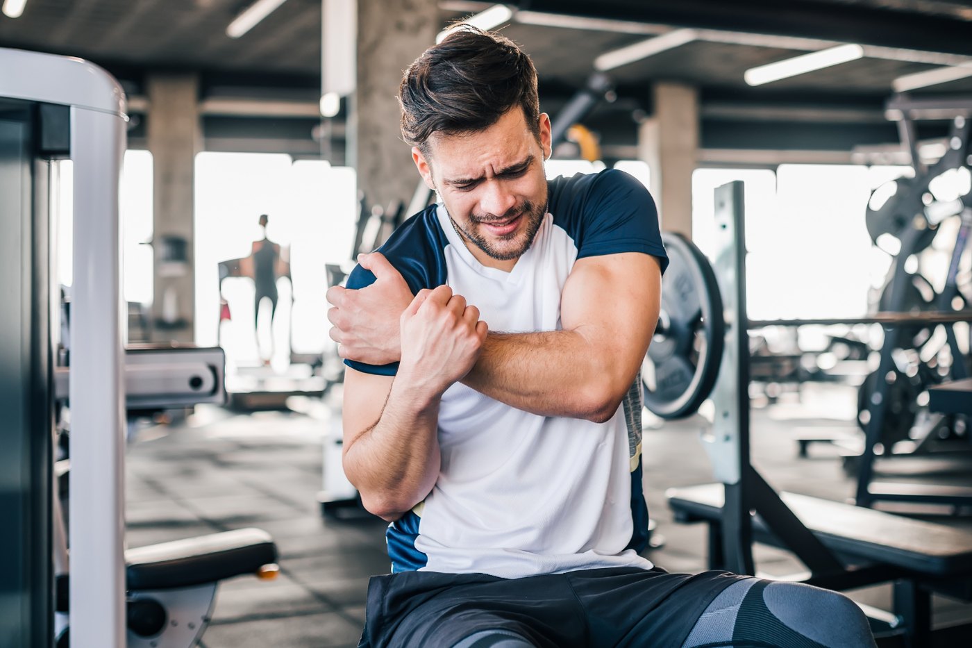 A man sitting in a gym holding his shoulder after a lift
