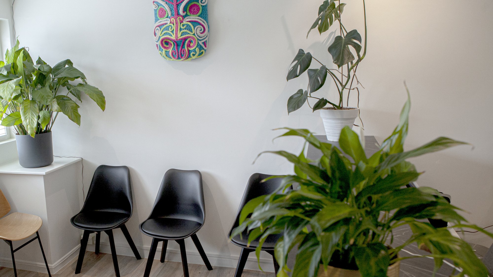 The waiting area at The Healing Centre Remuera: black chairs against a white wall, a carved Maori mask and large indoor plants